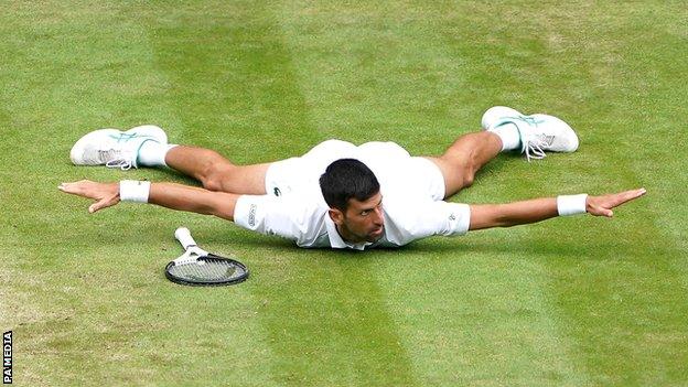 Novak Djokovic lies on his chest with arms and legs outstretched after winning a point in his quarter-final victory over Jannik Sinner