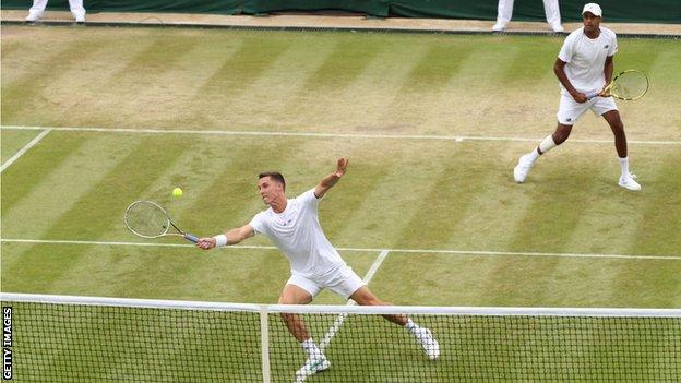 Joe Salisbury stretches for a volley with doubles partner Rajeev Ram