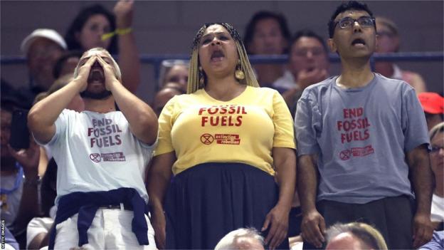 Protestors stand up wearing 'end fossil fuels' T-shirts during the US Open women's semi-final
