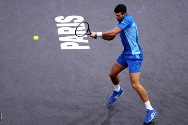 Novak Djokovic hits a backhand shot on the court which has the word 'Paris' engraved on it