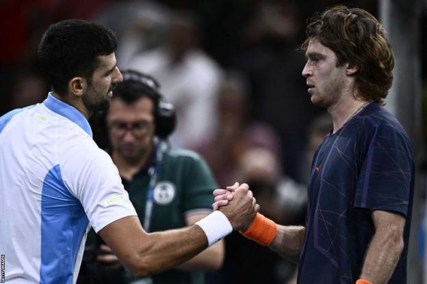 Novak Djokovic shakes hands with Andrey Rublev at the net